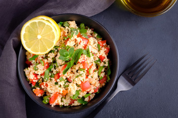 Tabbouleh salad in black bowl with grey napkin on black stone surface. Flat lay composition