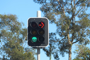 Modern traffic lights showing a green go signal and a red stop arrow. Trees and blue sky are in the...