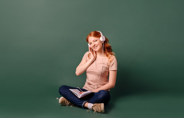 A young woman with red hair sitting reads a book and listens to music