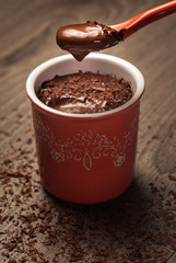 chocolate pudding in a red pot with cream on a spoon and chocolate chips on the grey table
