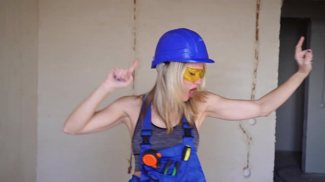 Young beautiful woman builder dancing indoors. Cheerful woman worker.