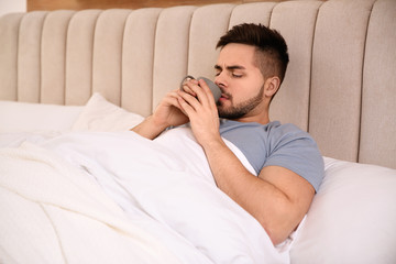 Sick young man with cup of hot drink in bed at home. Influenza virus