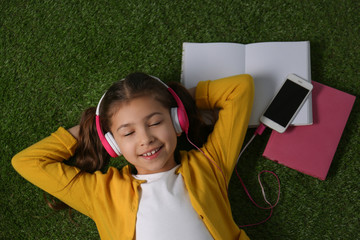Cute little girl listening to audiobook on grass, top view