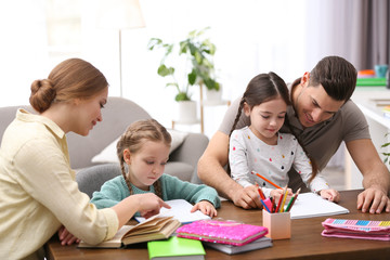 Parents helping their daughters with homework at table indoors