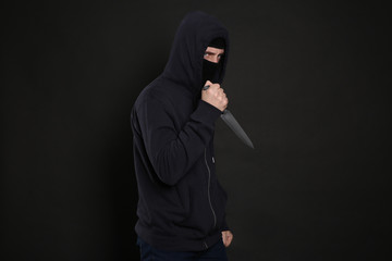 Man in mask with knife on black background. Dangerous criminal