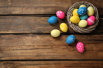 Fototapeta na wymiar Colorful Easter eggs in decorative nest on wooden background, flat lay. Space for text