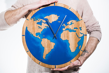 The wooden clock is filled with epoxy resin with a map of the world in the style of the LOFT. Man with clock on white background.