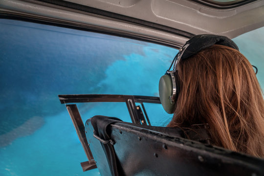 View from the helicopter during the flight. Young woman is looking on the coral reef of Cayman Islands. Excursion tour for the guests on a cruise ship in George Town. Red hair lady wearing headphones.