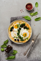 Turkish eggs flatbread with yoghurt, cheese, olives, spinach and red pepper on ceramic vintage plate on gray old background. Top view.