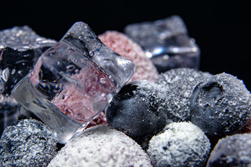 Macro view of frozen berries: strawberry, blueberry with ice cubes on dark background