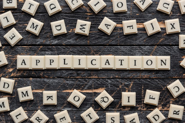 Application word made of square letter word on wooden background, random letters around.