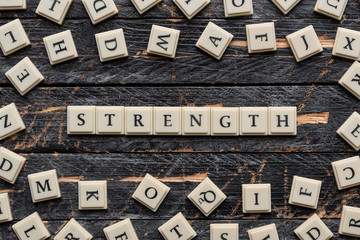 Strength word made of square letter word on wooden background, random letters around.