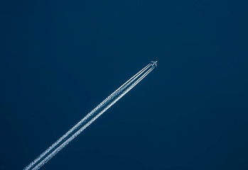 The plane leaves a white mark in the blue sky