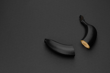 Two halves of a black banana on the matte black background. Minimal style. Conceptual minimalist black art. Matte surface. Cut fruit. One. Space for text