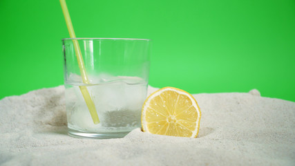 glass with ice and soda water and lemon on the sand on a green background