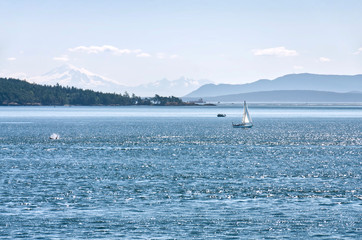 Sailboat on a background of turquoise sea water and mountains in a blue sunny haze. Sea landscape in bright colors. Strait of Georgia. Vancouver to Victoria Ferry trip