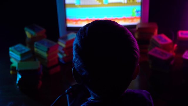 A little boy sits in front of the TV playing in a retro console. Neon lighting.Close up