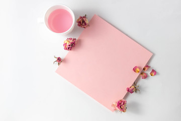 Empty pink sheet for writing and flowers on a white table. Top view, flat lay, copy space, minimalism. Space for adding text.