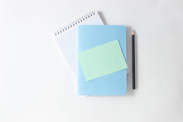 Notepads and empty green sheet for writing and flowers on a white table. Top view, flat lay, copy space, minimalism. Space for adding text.