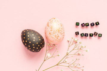 wooden painted eggs in gold, black and rose colors with branch of gypsophila on pink background. Happy easter text mde of black beads