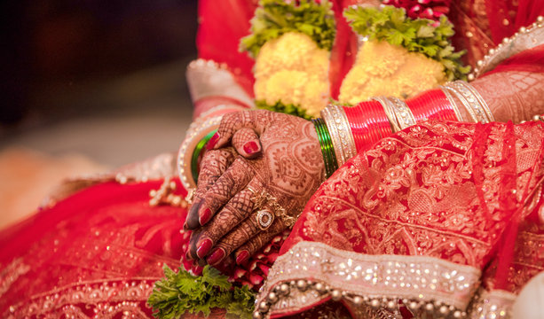 Beautiful photo of Indian bride in traditional wedding attire as per Hindu custom, wearing colorful bangles in hands decorated with henna mehndi is sitting with folded hands in her marriage ceremony.