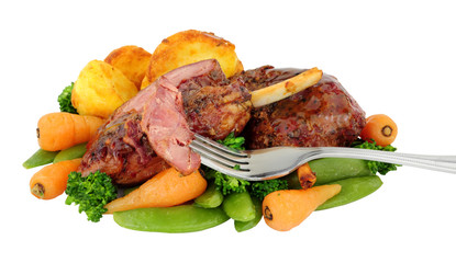 Slow cooked cured gammon shanks covered with caramelised maple sauce and roast potatoes, carrots, broccoli and sugar snap peas isolated on a white background