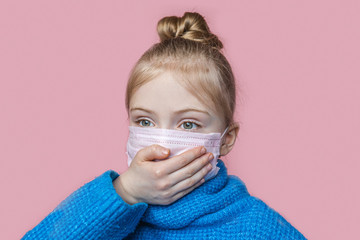 Danger of the virus. A small blonde girl in a gauze mask looks at the camera in fright and holds her hand on her face against a pink background.