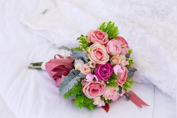 A beautiful bouquet of flowers was laid out on a clean, white bed. Next to the bridal gown were placed together.