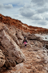 Small girl walks on the sea coast, she is wearing a coat, the kid travels along the sea, outdoor