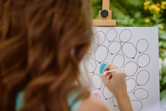 Girl or female artist with easel and paint brush painting balloons outdoors, copy space. Creativity and people concept