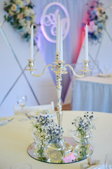 Beautiful floral arrangement and candles in candlestick on wedding table in restaurant, copy space. Bouquet of wildflowers in glass vase. Luxury wedding decorations