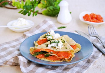 Thin crepe pancakes with salted salmon and cream cheese on a gray plate on a light concrete background. French cuisine. Pancake Day.