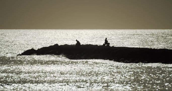 Two fishermen at a breakwater fishing at sunrise in the beach