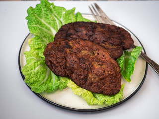 The sound of two cutlets of beef liver and lettuce, a plate on a white background