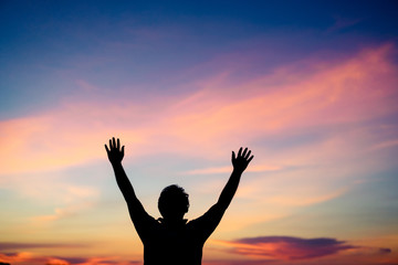 Silhouette man praying and worship to GOD on the sunset sky.Man praying to GOD in the morning.Young man hand praying,Raised Hands in prayer.Concept for faith,Praise the lord spirituality and religion.