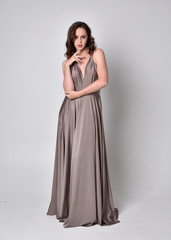  Portrait of a pretty brunette girl wearing a long silver evening gown, full length standing pose...