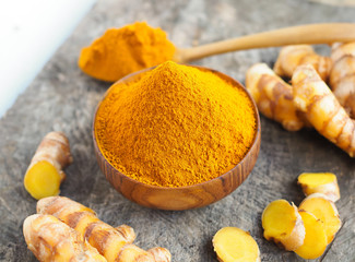 Turmeric powder and fresh turmeric in wood bowl on old wooden table. Herbal