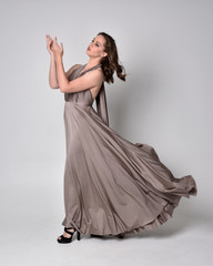  Portrait of a pretty brunette girl wearing a long silver evening gown, full length standing pose...