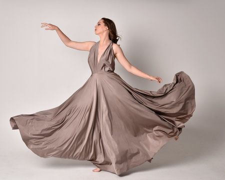  Portrait of a pretty brunette girl wearing a long silver evening gown, full length standing pose against a studio background.