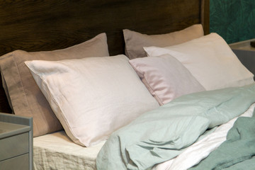 Close- up of a new mint- colored blanket with decorative pillows, wooden headboard in bedroom in sample model of house or apartment