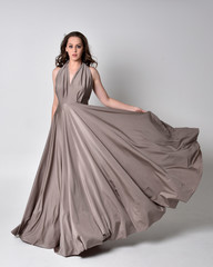  Portrait of a pretty brunette girl wearing a long silver evening gown, full length standing pose...
