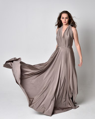  Portrait of a pretty brunette girl wearing a long silver evening gown, full length standing pose...