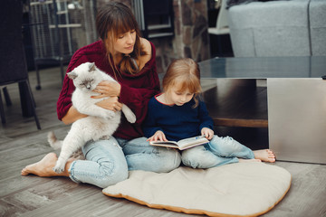 Beautiful mother with little daughter. Family sitting in the room. Cute girl doing homework. Woman...