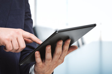 Businessman holds digital tablet and clicks on screen in modern office, close up. Search concept