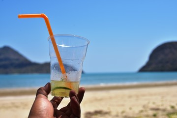 A glass of lemonade in hand with a sea view with a sea view and blue sky