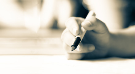 Close up business hand holding pen for signing on paper contract making a deal, vintage monotone...