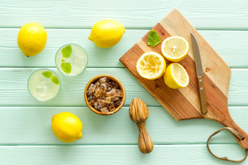 Homemade lemonade in glasses near juicer and cut lemons on green wooden background top-down