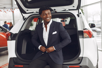 Man buying the car. Businessman in a car salon. Black male in a suit.