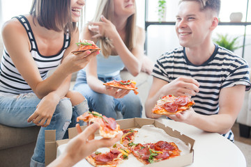 Young people eating pizza. Group of friends having lunch indoors. Funny friends together.