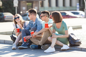 Group of young people near the fountain drinking coffee and having fun. friends relaxing outdoors.